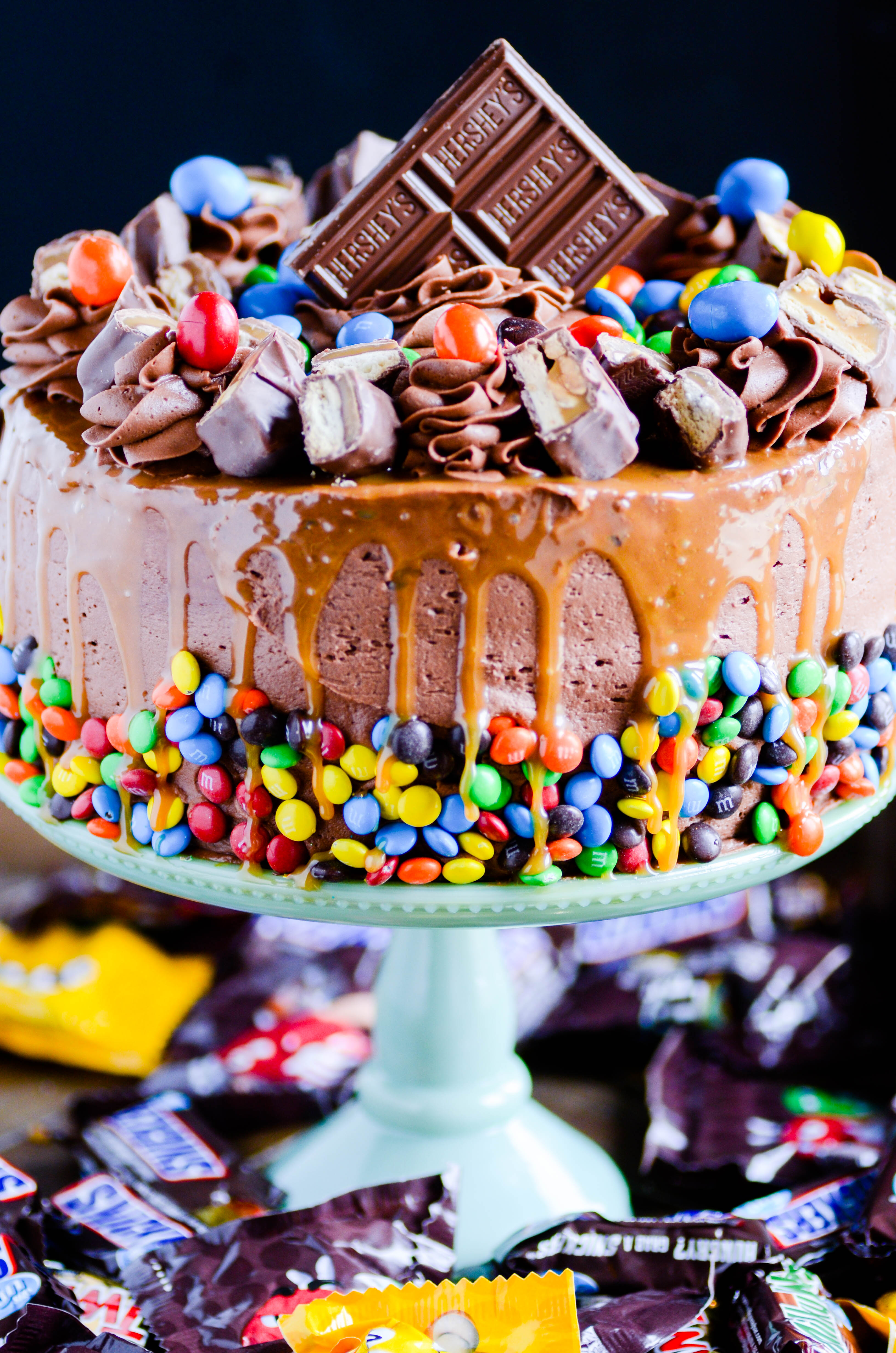 This chocolate cheesecake cake is completely over the top! A layer of cheesecake smothered in a layer of caramel and peanuts sandwiched in between two thick layers of my favorite chocolate cake. Frosting with the BEST chocolate frosting of all time and topped with candy bars and a caramel drizzle.